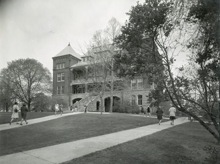 The front of Catt Hall. The lawn and surrounding foliage is featured in the foreground. Several individuals in period clothing are walking on the sidewalks in front of Catt Hall. This image is part of a set of images that includes: w 4-8-I.CattHall.234-4-3-2.