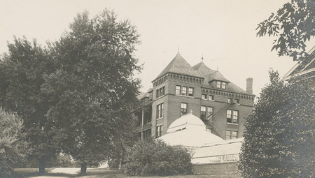 The side of Catt Hall and the greenhouse building beside it. The surrounding foliage obscures parts of both buildings.