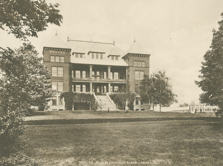 The front of Catt Hall with the greenhouse to the right. Trees in the foreground frame the scene.