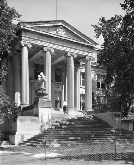 A man walks up the steps of Curtiss Hall, which has a chain link fence in front of it.