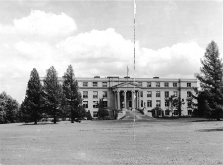 The front (west) facade of Agriculture Hall (Curtiss Hall) is framed by three large pine trees on the north and one on the south.