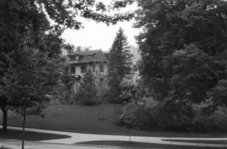 A view of the Knoll undergoing renovation and expansion. A scene is framed in trees. A sidewalk and street run across the foreground of the frame.