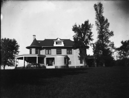 This eastern view of the Knoll shows the large wrap around porch on the left and the porte cochere on the right. The large lawn is in the foreground and trees surround part of the building.