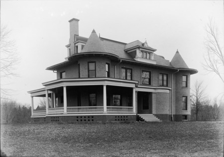 The southeast corner of the Knoll dominates this ground level view. The entryway and wrap-around porch are in the center of the frame with the lawn in the foreground.