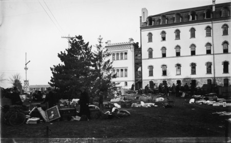 The south wall of the south wing of Old Main after the fire in December 1900. Large amounts of building contents are on the grounds. People near the building are looking through the remains.