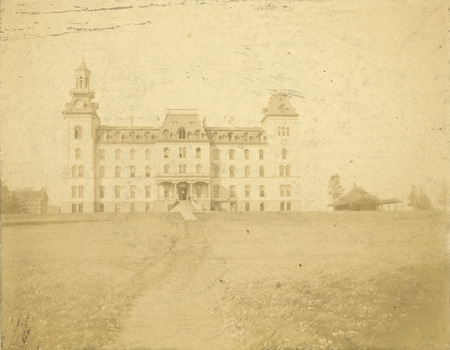 The front side of Old Main with a great expanse of central campus in front of the building. The Hub building located north of Old Main is also in the view.