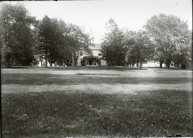 Photograph of the front of the Farm House showing the lawn in front of the house. Annotation: “Farm House. Horse & Cattle barns in background on right. n.d.”