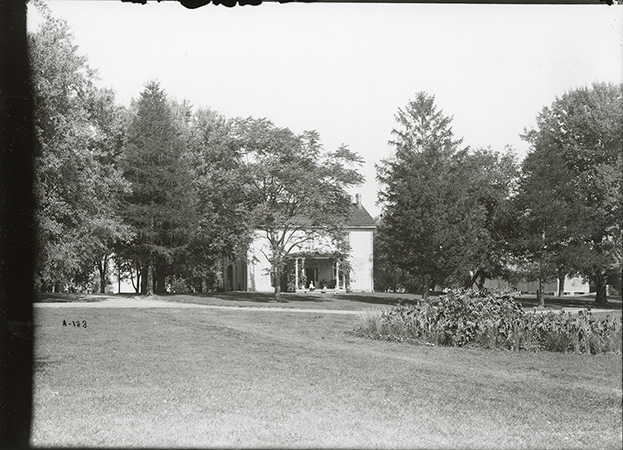 Photograph of the south side of the Farm House showing the front porch. The Cattle Barn, First can be seen in the background to the right (north-east) of the Farm House. Annotation: “Farm House. Cattle barns in background. Sept. 22, 1905 from south.”