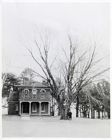Photograph of Sloss House in the winter. A person stands beside a tree in the snow.