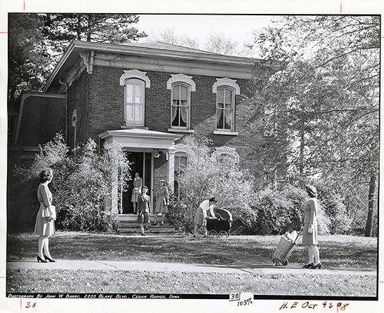 Photograph of women outside Sloss House while it was being used as a home management house. One woman leans over a baby carriage, while others stand on the steps and sidewalk.