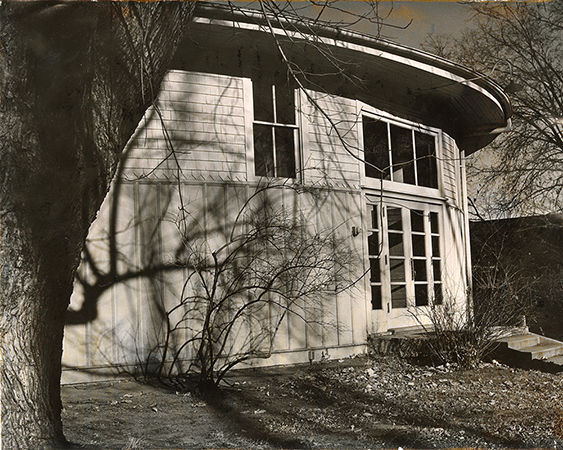 Photograph of the south doors of the Shattuck Theatre. There are trees and bushes without leaves in the foreground. 