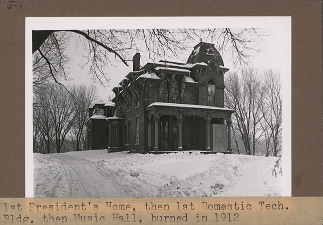 Photograph of South Hall on the Iowa State campus in winter, showing the north and west elevations. The view looking is southeast. The image depicts a large brick building with a covered porch, surrounded by snow and leafless trees. Annotation: ''1st President's Home, then 1st Domestic Tech. Bldg., then Music Hall, burned in 1912. Music Hall (Old South Hall) Built in 1869, burned in 1912. South Hall, Green Hills, p. 20.''