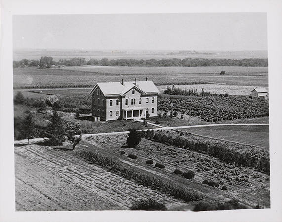 Photograph of North Hall on the Iowa State campus, viewed from Main looking northeast. The image shows a brick building situated within an agricultural landscape, surrounded by cultivated fields, garden plots, and open land. Annotation: "North Hall, neg 05123."
