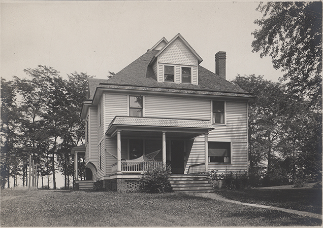 Photograph of Norton House on the Iowa State campus, showing the front and side elevations of a two-story residence. The building features a front porch with columns, a dormered roof, and a hammock visible on the porch. The house is situated among scattered trees in the surrounding landscape. Annotation: "Norton House. The Coover House on campus."