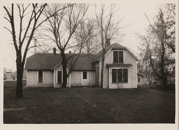 Photograph of the first creamery building, facing east. In the left background, the judging pavilion and the power plant are visible. The creamery is a one-story building. Leafless trees are in the foreground.