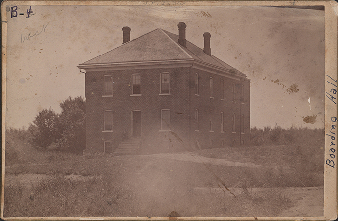Photograph of two sides of West Boarding Cottage. It is a two story brick building, with three chimneys visible.
