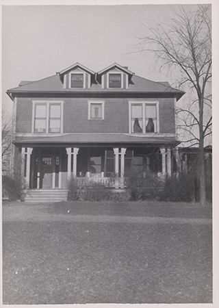 Photograph of Bevier House from the front. It has a front porch with bushes in front. The trees and bushes do not have leaves. The caption reads "Sloss Family lived here from 1910-1925."