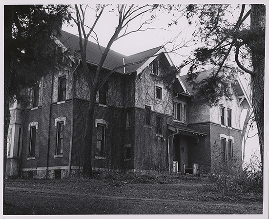 Photograph of International House showing one side and the front of the house. Ivy vines cover the front, and leafless trees are in the foreground.