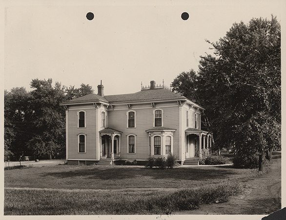 Photograph of Mortensen Cottage. The photo is a side view of the house. It is a two-story house with a front porch and a side entry. A bay window is visible on the side of the house. The caption reads "Old residence of Prof. J. L. Budd onsite of the present Old. Ag. Hall, just outside the limits of the circle, on slight elevation directly north of the campanile. The building is at present located just north of the Dairy building. After being occupied by Prof. Budd it was occupied by Prof. McKay and is now occupied by Prof. Mortensen."