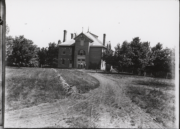 Photograph showing three people standing outside the north side of the Veterinary Hospital. Annotation: ''Veterinary Hospital view from north early 1900s?''