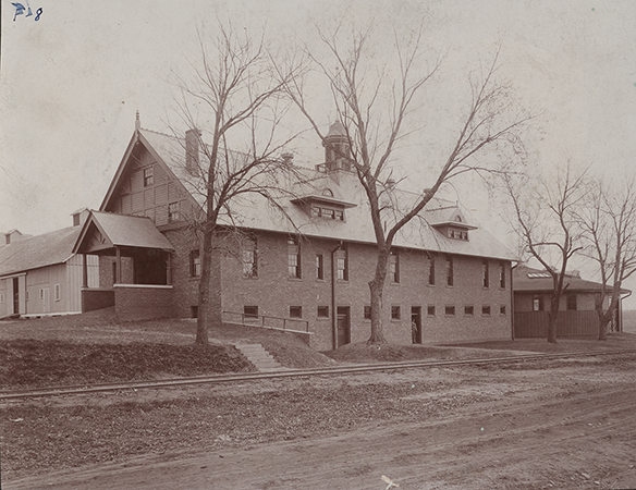 Photograph of the southwest corner of Landscape Architecture when it was the Horse Barn. The Cattle Barn can be seen to the north (left), and the Theater Workshop (when it was the Judging Pavilion) can be seen to the east (right). Dinky tracks run along the south (foreground) of the buildings.
