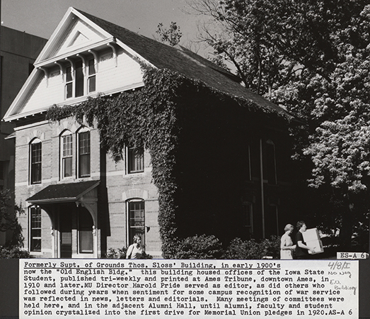 Photograph of three people walking past the northeast corner of the English Office Building. Part of Carver Hall can be seen to the south (left). Annotation: ''Formerly Supt. of Grounds Thos. Sloss' Building in early 1900's now the "Old English Bldg" this building housed offices of the Iowa State Student, published tri-weekly and printed at Ames Tribune, downtown Ames, in 1910 and later. MU Director Harold Pride served as editor, as did others who followed during years when sentiment for some recognition of war service was reflected in news, letters and editorials. Many meetings of committees were held here, and in the adjacent Alumni Hall, until alumni, faculty and student opinion crystalized into the first drive for Memorial Union pledges in 1920.''