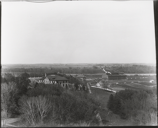 Photograph looking northeast past East Hall and down the Fort Dodge, Des Moines and Southern Railway tracks. In the distance a piece of the Carpenter Shop (Judging Pavilion #3) can be seen to the left of the tracks and the Power and Heating Plant can be seen behind where the tracks curve east. Annotation: ''East Hall, judging pavilion, power & heating plant, hog house. May 5, 1913.''