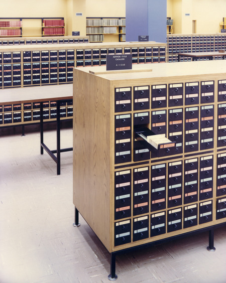 A drawer of the author-title catalog is pulled out, with more catalog cabinets and tables in the background, and bibliographies on shelves on the wall.