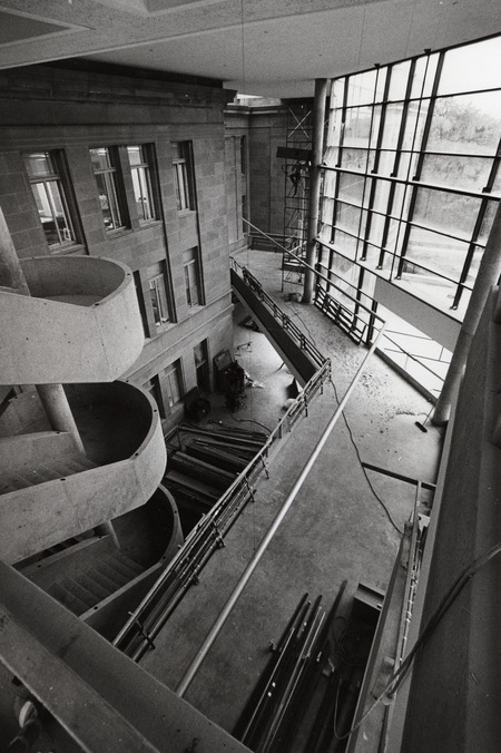 An in-progress view of the 3rd Addition construction looking down from the fourth floor to the second floor bridge, with the circular main staircase and old building facade on the left.