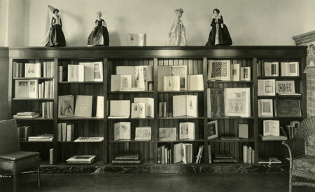 Figurines dressed in historic costumes are displayed on the top of bookshelves in this Veishea book exhibit located in the Library Staff Lounge (currently called the Fireplace Room).