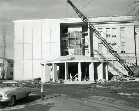 The 1st addition to the library is being constructed with a rotunda entrance on the south side. A large crane is on the right and a mid 1950's Studebaker is parked on the left.