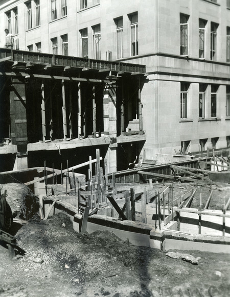 The concrete foundation and two levels of the 1st addition are under construction. Vertical rebars and wooden planks are sticking up from the foundation.