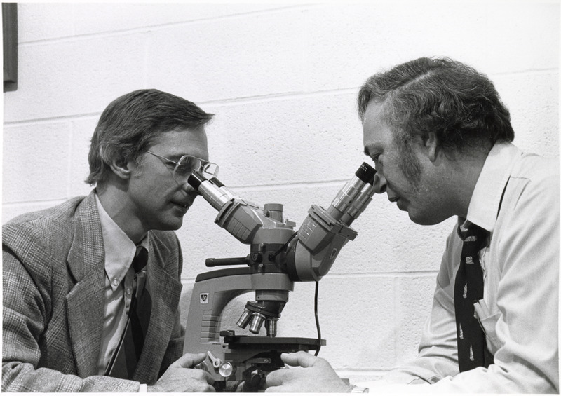 Photograph of John Kluge and Russell Kemp using a microscope to examine a specimen