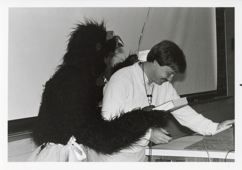 Photograph of James Noxon receiving a gift from a student in a gorilla costume on his birthday