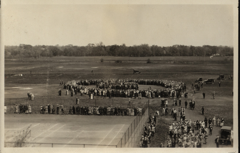 Photograph showing a crowd gathered around a bonfire burning freshman beanies.