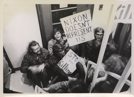 Students participating in a sit-in demonstration at a local selection services draft board. Their signs read, "Nixon Doesn't Represent Us" and "Stop The Killing.".
