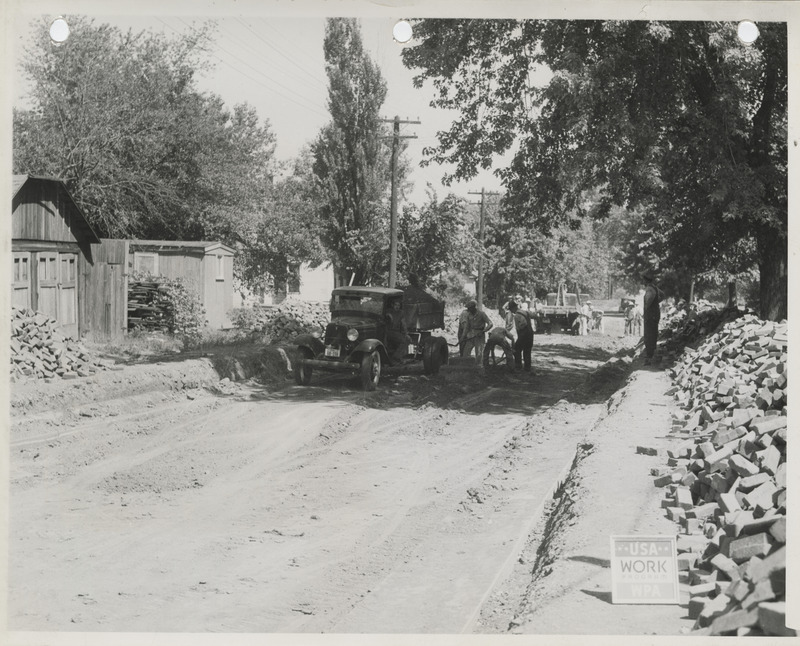 Photograph of people lowering a street level and paving it with bricks in Albia