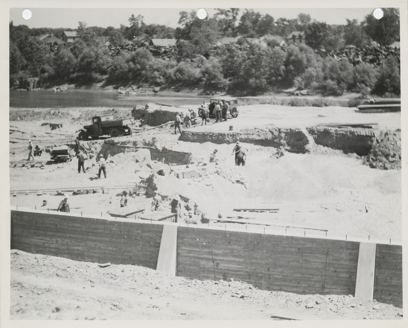 Photograph of people removing dirt from the front of a river wall on the Raccoon River in Des Moines