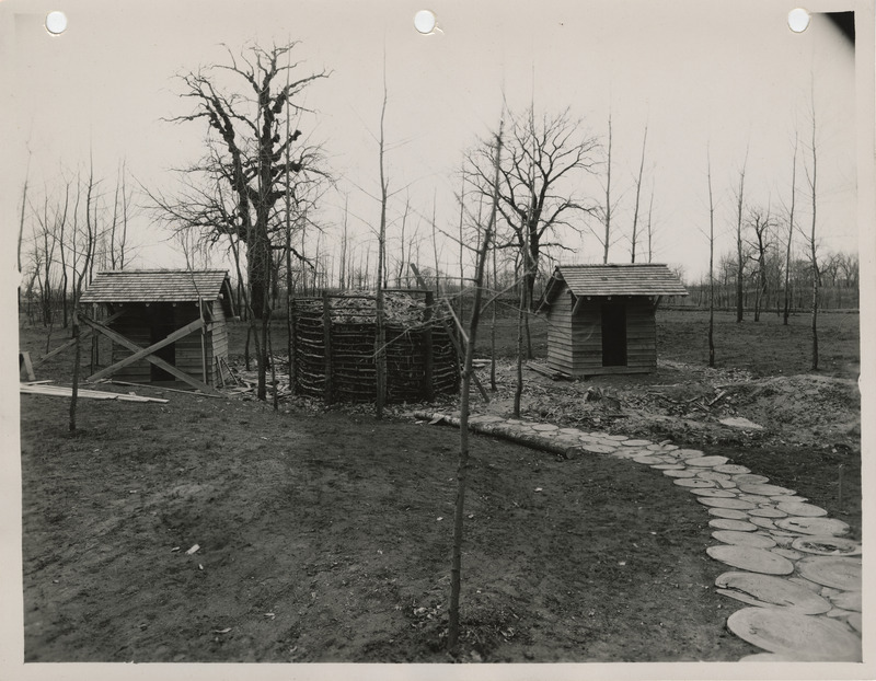 Photograph of latrines, crib for storing wood shavings and sidewalk in the Lewis and Clark State Park