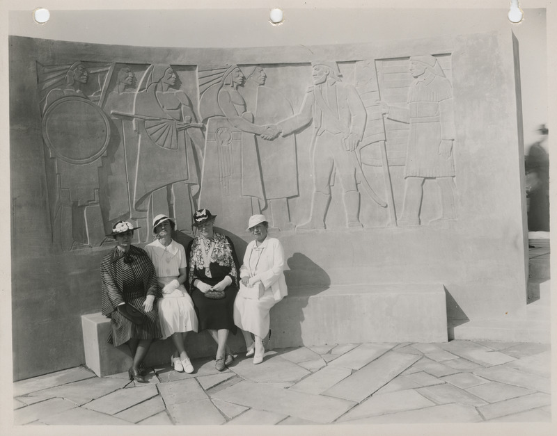 Photograph of four people sitting in front of the Lewis and Clark monument in Council Bluffs