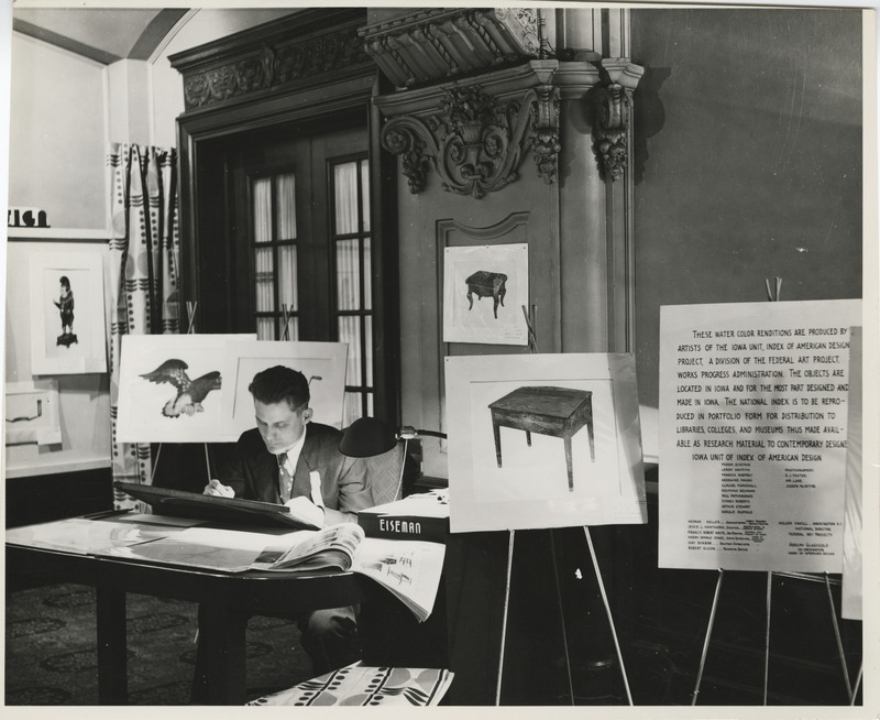 Photograph of a person sitting at a desk surrounded by watercolors depicting Iowa objects