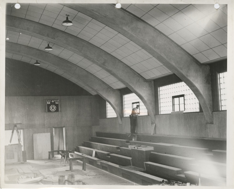 Photograph of a person working on bleachers in a school gymnasium in Luverne